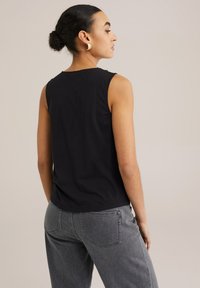 Črna brezrokavna majica z ohlapnim krojem, v kombinaciji s sivo visokim pasom. Tkanina se zdi mehka z minimalnimi šivi.