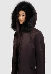 Sort puffjakke med hætte beklædt med pels, store frontlommer og en lomme med lynlås på ærmet. Glat, blankt stof med en skræddersyet pasform.