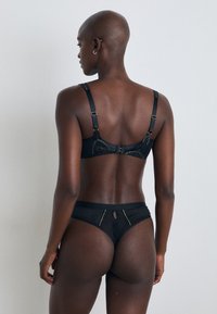 Conjunto de lingerie preto com um sutiã de design em malha transparente e costura decorativa, e calcinha combinando com recorte e detalhes em ouro.