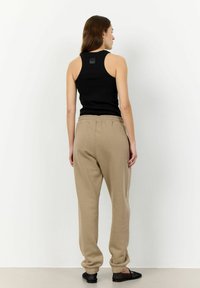 Schwarzes geripptes Tanktop mit rundem Halsausschnitt, kombiniert mit lockeren beigen Sweatpants mit elastischem Bund und Bündchen.