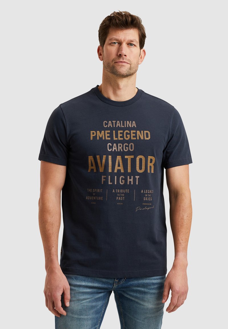 Navyblauwe katoenen t-shirt met korte mouwen, met gouden tekst en grafische ontwerpen. Casual pasvorm, ronde hals; gedragen met blauwe jeans.