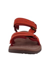 Teva sandals with orange textile straps, adjustable hook-and-loop closures, and a brown cushioned sole, designed for comfort and stability.