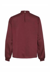 Blouse bordeaux à manches longues avec col et poignets froncés, fermeture au dos par bouton à œillet, tissu lisse, sans décorations visibles.