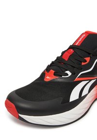 Melnas sporta kurpes ar sarkaniem akcentiem, tīkla auduma augšdaļa, ar auklām saistāma dizaina un izliekta balta un sarkana zole, kas nodrošina amortizāciju.