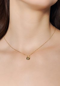 Złoty naszyjnik z teksturowanym zawieszeniem w kształcie kropli na cienkim łańcuszku, spoczywający na gładkiej skórze. Prosty design, niezdobiony dodatkowymi akcentami.