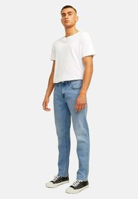 Jeans in denim azzurro chiaro con una vestibilità dritta, abbinati a una semplice maglietta bianca in cotone e sneakers nere con lacci bianchi.