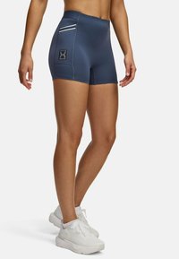 Marineblaue Sportshorts mit hoher Taille, schlankem Design, weißen Akzentstreifen und einem Markenpatch an der Seite. Hergestellt aus dehnbarem Material.
