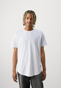 Hvid bomulds-t-shirt med korte ærmer, rund hals og buet kant. Stoffet ser glat og let ud, designet til afslappet brug.