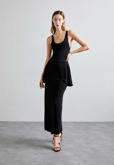 Mustat ilmanhihaiset mekko, jossa on tiukka siluetti ja peplum-yksityiskohta vyötäröllä, valmistettu sileästä kankaasta; yhdistetty mustiin hihnakengiin.