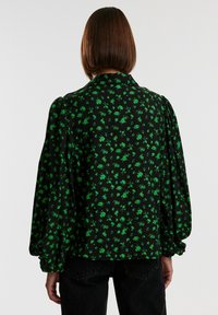Blusa nera con stampa floreale verde; ha maniche a sbuffo e colletto, realizzata in tessuto leggero; mostrata da dietro.