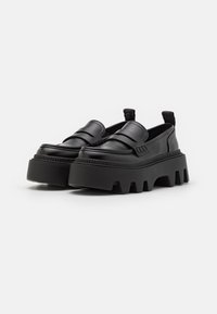 Melnas platforma loafer kurpes, kas izgatavotas no gludas ādas, ar elastīgām sānu daļām, masīvu gumijas zoli un diskrētām šuvju detaļām.