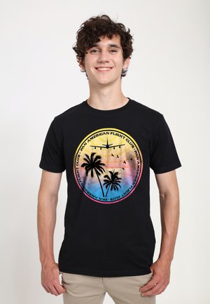 Black t-shirt featuring a graphic design with palm trees, an airplane, and colorful sunset gradients; round logo text "Pan American Flight Club."