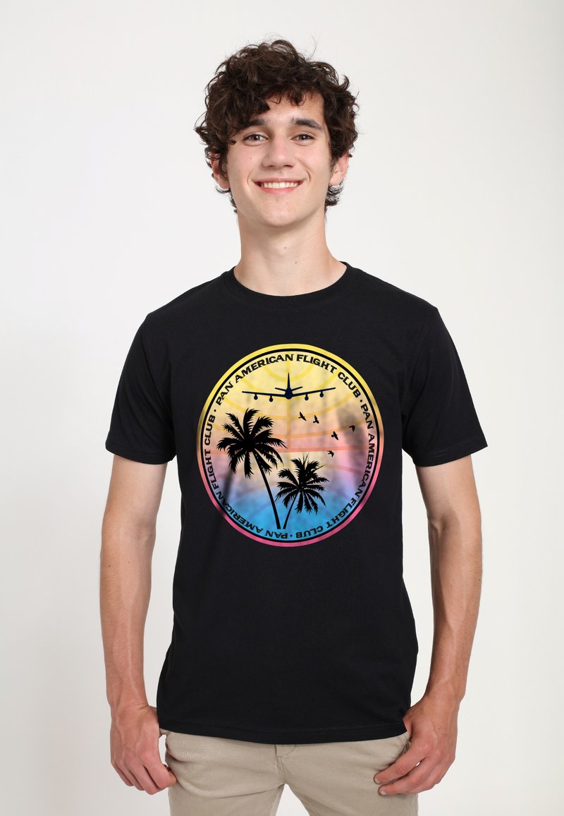 Sort t-shirt med et grafisk design, der inkluderer palmer, et fly og farverige solnedgangsgradienter; rund logo-tekst "Pan American Flight Club."