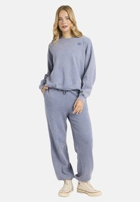 Sudadera azul clara y pantalones de chándal a juego con una textura suave y cepillada. Presenta un cuello redondo y una cintura con cordón ajustable.