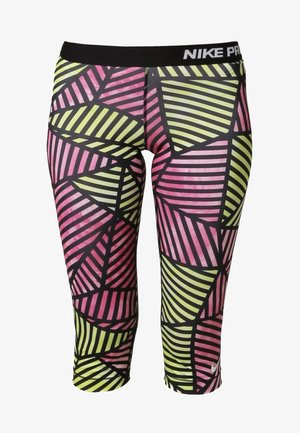 Frau trägt ein weißes Tanktop, mehrfarbige geometrische Capri-Leggings und neon-gelbe sowie weiße Sneakers, sie geht mit leicht gesenktem Kopf.