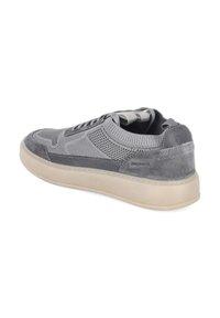 Zapatilla deportiva gris de corte bajo con parte superior de punto y ante, suela beige y lengüeta, vista desde atrás y en ángulo lateral.