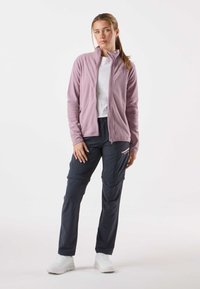 Jasnofioletowa polarowa kurtka z pełnym zamkiem błyskawicznym, zestawiona z ciemnogranatowymi spodniami cargo z kieszeniami i zamkiem błyskawicznym jako akcentem. Białe trampki.