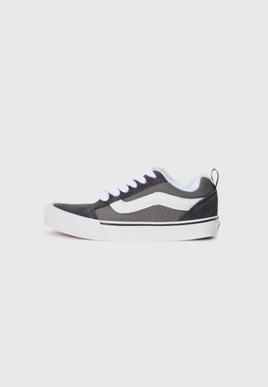 Schwarze und graue Leinensneaker mit weißen Akzenten, die über eine abgerundete Zehenpartie, flache, weiße Schnürsenkel, eine Fersenlasche und eine Gummisohle verfügen.