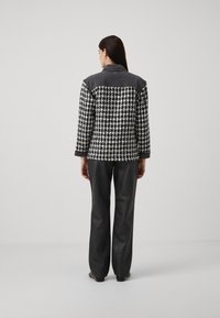 Sako s čierno-bielym vzorom houndstooth a šedým denimovým golierom, skombinované s tmavošedými širokými nohavicami. Hladká textúra, štruktúrovaný strih.