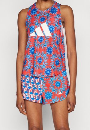 Sportowy top bez rękawów i szorty z czerwono-niebiesko-białymi geometrycznymi i kwiatowymi wzorami na tułowiu i nogach osoby.