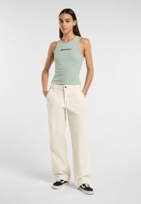 Top aderente a costine verde menta con logo nero, abbinato a pantaloni larghi crema e sneakers nere, con una vestibilità rilassata.