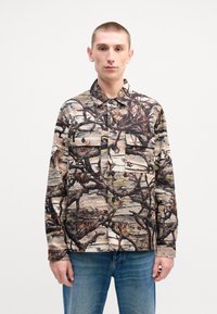 Camo-patterned shirt with a button-up design, featuring two chest pockets, made of fabric with beige, brown, and dark green tones.