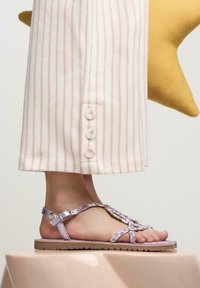 Sandali viola con cinghie e accenti floreali, suola piatta e fibbia regolabile. Abbinati a pantaloni a righe rosa chiaro con dettagli in bottone.