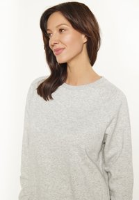 Felpa grigia chiaro con collo a giro, maniche raglan e texture morbida. Caratterizzata da cuciture minime e vestibilità rilassata.