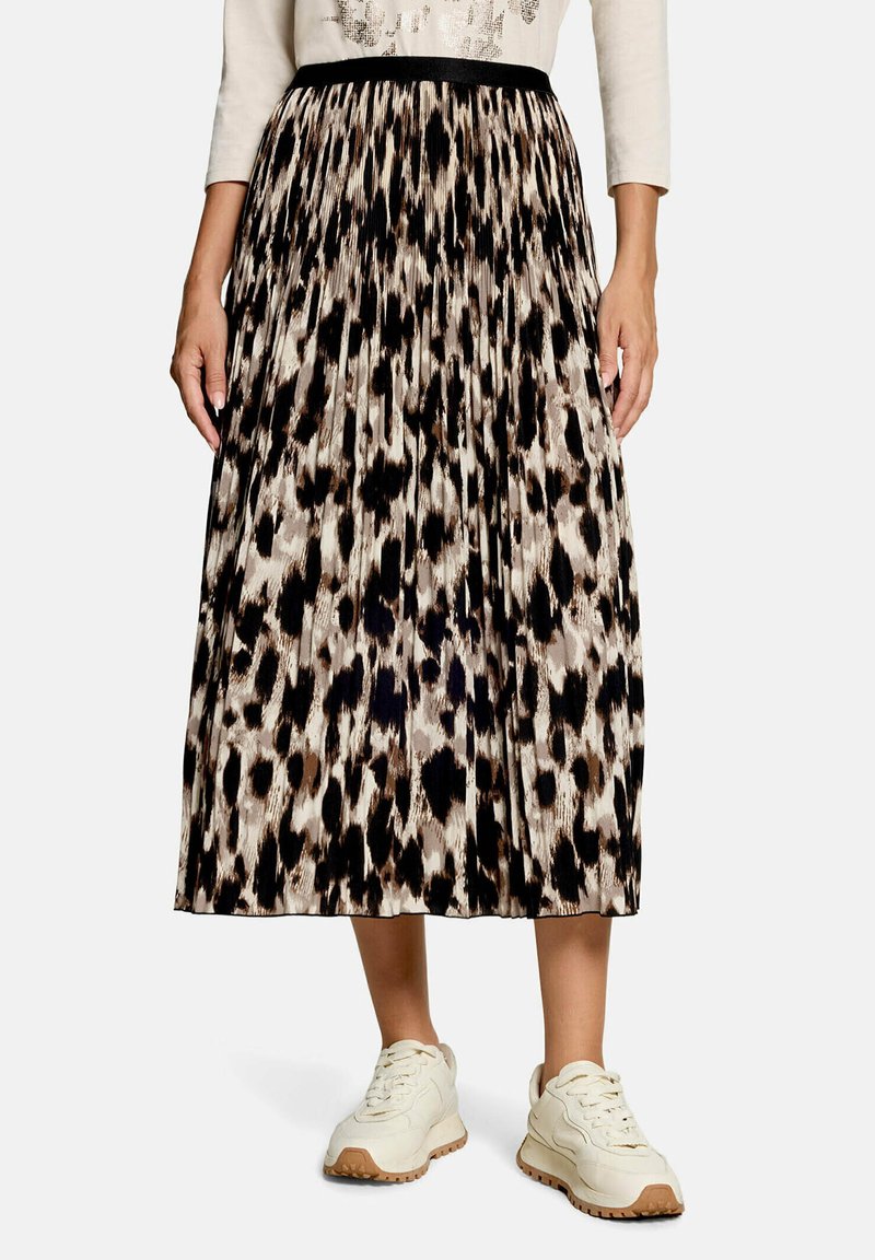 Personne portant une jupe midi plissée à imprimé animalier avec une ceinture noire, un haut à manches longues écru et des baskets blanches avec semelles en gomme.