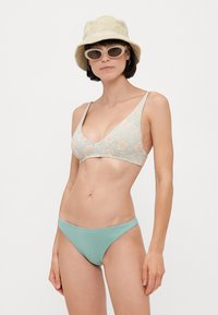 Blomsterbikini topp i lys grønn med ferskenfargede detaljer; matchende ensfarget lyseblå bunn. Teksturert stoff, trekantet snitt, minimal dekning.