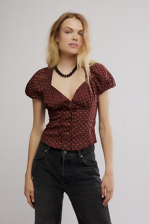 Burgundy puff-sleeve blouse with gold dot pattern, tying front, and button closure, paired with high-waisted black jeans.