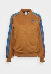 Veste zippée marron avec un motif de feuilles texturé, rayures bleues sur les épaules, poignets élastiques et bord-côte. Logo Adidas sur la poitrine.