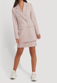 Vestido tipo blazer en rosa claro con patrón de cuadros, diseño cruzado, solapas anchas y dos bolsillos delanteros, combinado con zapatillas blancas.