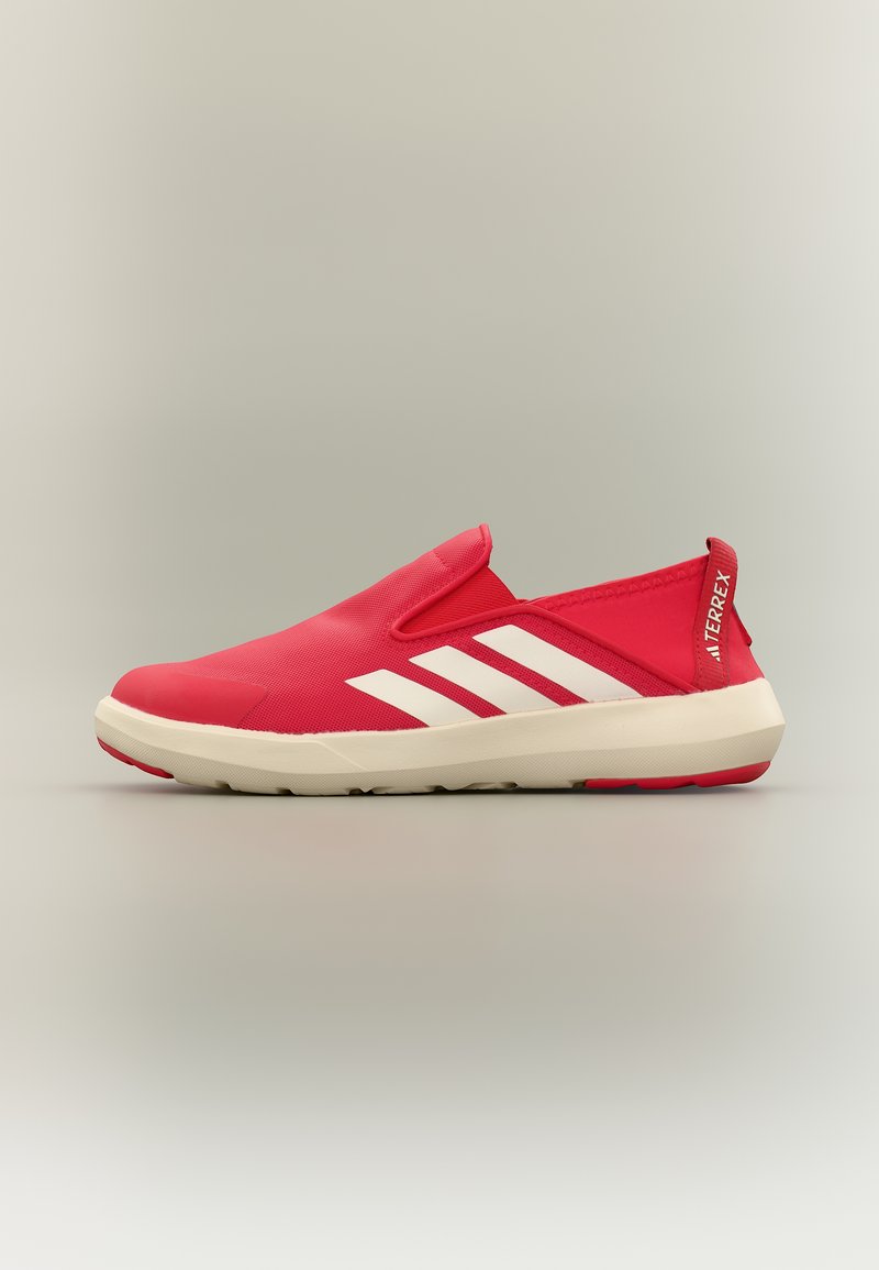 Κόκκινο αθλητικό παπούτσι τύπου slip-on με λευκή σόλα και τρεις λευκές ρίγες, με σήμανση "TERREX" στην πίσω γλώσσα.