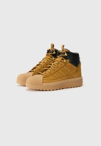 Δερμάτινα μπότες σε καφέ suede με μαύρη δερμάτινη λεπτομέρεια. Διαθέτουν ραβδωτή καουτσούκ σόλα και χρυσές λεπτομέρειες για τα κορδόνια. Ορατό μαλακό ύφασμα επένδυσης.