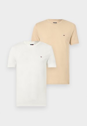 Kaksi yksiväristä pyöreäkaulaista t-paitaa, yksi valkoinen ja yksi beige, kummassakin pieni Tommy Hilfiger -logo vasemmassa rinnassa.