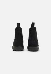 Bottines en daim noir avec une finition texturée, dotées d'une semelle en caoutchouc robuste et de poignées à l'arrière pour un enfilage facile.