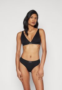 Mustat saumattomat bralette-risti, jossa on syvä V-kaula-aukko ja säädettävät hihnat, yhdistettynä yhteensopiviin korkeavyötäröisiin alusvaatteisiin. Minimalistinen muotoilu logotarkoituksella.