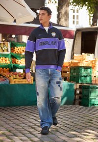 Sort og lilla hættetrøje med lynlås og "REPLAY" logo, parret med slidte blå jeans og sorte sneakers. Markedsscene med frugttræer.