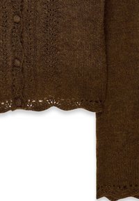 De bruine gebreide cardigan heeft een gestructureerd patroon, een scalloped zoom en knopen langs de voorkant, wat de zachtheid en warmte benadrukt.