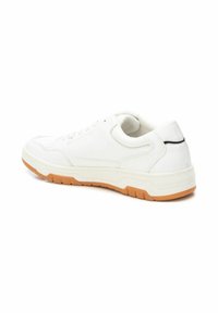 Zapatilla blanca con un upper de cuero liso, cuello acolchado y suela de goma que presenta un acento naranja a lo largo del borde inferior.
