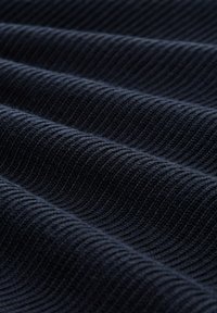 Tissu texturé bleu foncé avec un motif ribbé, présentant des rayures alternées en relief et plates, évoquant profondeur et dimension.