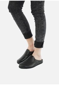 Des chaussures noires à enfiler en cuir texturé, avec un bout rond et un design bas, associées à un jean foncé et ajusté.
