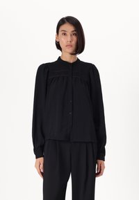 Black blouse with a collar, button front, and gathered details. Long sleeves with elastic cuffs. Soft fabric with a slight sheen.