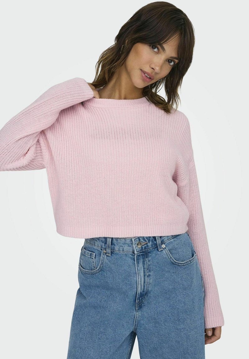 Maglione lavorato a maglia rosa chiaro con un design corto, scollatura ampia e maniche lunghe, abbinato a jeans in denim blu a vita alta.