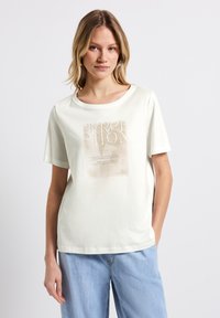 T-shirt en coton crème clair avec une coupe décontractée, un col rond et des manches courtes. Présente un imprimé graphique texturé dans des tons beiges.
