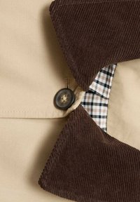 Bežna srajca s stožčastim ovratnikom v rjavi barvi, z gumbnim zapiranjem in podlogo s karirastim vzorcem v črni in beli barvi. Mehka tekstura.
