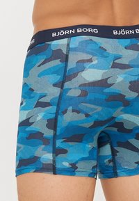 Boxershorts im blauen Camouflage-Muster. Hergestellt aus weichem Material, mit einem dunklen Bund, der das Logo "BJÖRN BORG" trägt, schmaler Passform und flachen Nähten.