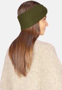 Bandeau vert en tricot, confectionné en matériau doux avec un design torsadé, porté par une personne aux cheveux bruns, assorti à un pull beige clair.