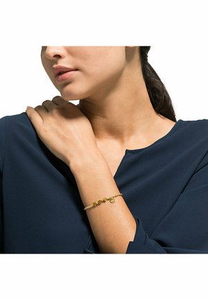 Goldenes Armband mit runden und herzförmigen Charms, strukturiertes Kettenglied, am Handgelenk getragen, neben einer marineblauen Bluse.